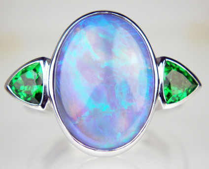 Oval black opal & tsavorite garnet ring - Beautiful strikingly coloured green and blue coloured 6.50ct black opal oval cabochon from Lightning Ridge, Australia rubover set in 18ct white gold and flanked by a 0.94ct matched pair of trillion cut tsavorite garnets, also rubover set. The stones are mounted on a Fingermate opening shank to accommodate larger knuckles and slender fingers. Ring size M.