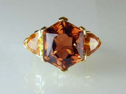 tourmaline - 9.66ct hexagonal cut deep golden brown tourmaline of exceptional clarity flanked by a 3.07ct matched pair of trillion cut mandarin garnets from Nigeria set in a handmade 18ct yellow gold ring