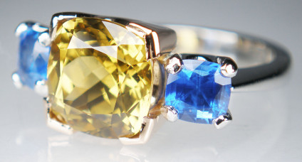 Chrysoberyl & sapphire ring - Set in platinum and 18ct rose gold in this striking ring, there is a 4.98ct cushion cut yellow chrysoberyl, flanked by a 1.61ct matched pair of fine blue cushion cut sapphires