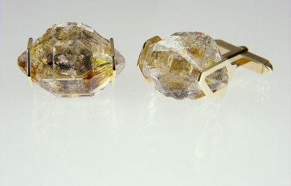 Oil included quartz cufflinks in gold - Cufflinks in 9ct yellow gold, larger crystals. Rare oil included quartz crystals from Balochistan are set in individually handmade gold mounts.  The crystals are approximately 2-3cm in all dimensions and contain golden droplets of light oil, along with darker bitumen and an aqueous solution.  The inclusions fluoresce a strong bluish green under UV light.  Each pair of cufflinks comes with a UV pen torch and an explanation of the crystal.  These crystals are extremely rare and it is difficult to find such perfect examples as sold by Just Gems.  The setting is precisely made to fit each unique crystal and has to be created without the application of heat, which could cause the crystal to fracture.  Each piece is handmade in Scotland and hallmarked in Edinburgh. Pendants and earrings also available.  A selection of crystals are available for bespoke designs.