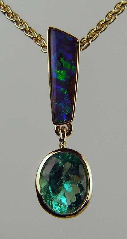 Emerald & Opal Pendant - Oval Colombian emerald rubover set in 18ct yellow gold and suspended from a fine sliver of blue/grey Australian boulder opal, mounted on an 18" 18ct yellow gold spiga chain