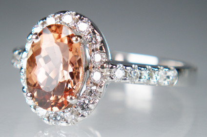 Brazilian imperial topaz and diamond ring in white gold - 1.97ct oval cut Brazilian imperial topaz  surrounded by a halo of round brilliant cut white diamonds and with diamond set shoulders. Total diamond weight is 0.47ct. The ring is made in 18ct white gold