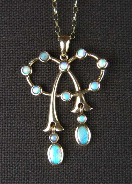 Opal pendant in 9ct yellow gold - Delicate and pretty opal pendant set with 8 x 2.5mm round solid white opals and two pairs of oval/round opals as moving drops to the tails of the bow. This is an antique piece but has, at some time in the more recent past, been hallmarked as 9ct. The piece measures 27mm wide by 40mm long and is suspended from a fine 9ct 21" gold chain. 