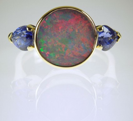 Black opal & sapphire ring - Opal and sapphire ring in 18ct yellow gold.  Round 1.45ct opal cabochon with red, green and blue colours, bezel set and flanked by a 1.55ct matched pair of sapphire pear cuts.
