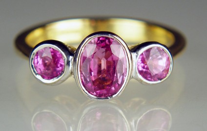 Pink sapphire 3 stone ring - Faceted pink sapphire three stone ring with a central 7 x 5mm oval flanked by a pair of 4mm rounds totalling 1.65ct, and rubover set in 18ct yellow and white gold