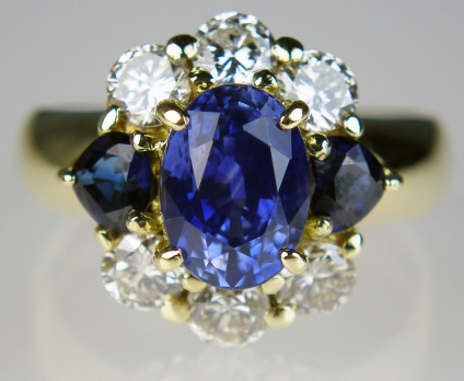 Sapphire & diamond cluster ring in 18ct yellow gold - Spectacular sapphire & diamond cluster ring in 18ct yellow gold. The central oval sapphire is 2.31ct and the matched flanking pair of darker trillion cut sapphires weigh 1.25ct, there are also 0.76ct of round brilliant cut diamonds top and bottom.